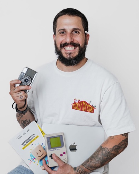 Portrait de Ludo, souriant, avec un appareil photo, un livre sur les usages du numérique, une Game Boy et un ordinateur portable.